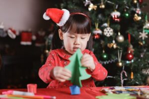 Toddler in a Santa hat making a green paper Christmas tree craft at a table