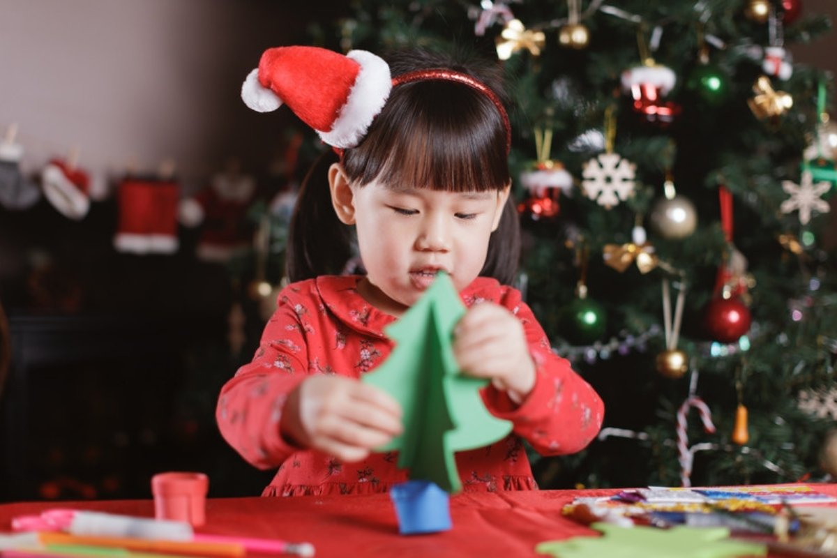 Toddler in a Santa hat making a green paper Christmas tree craft at a table