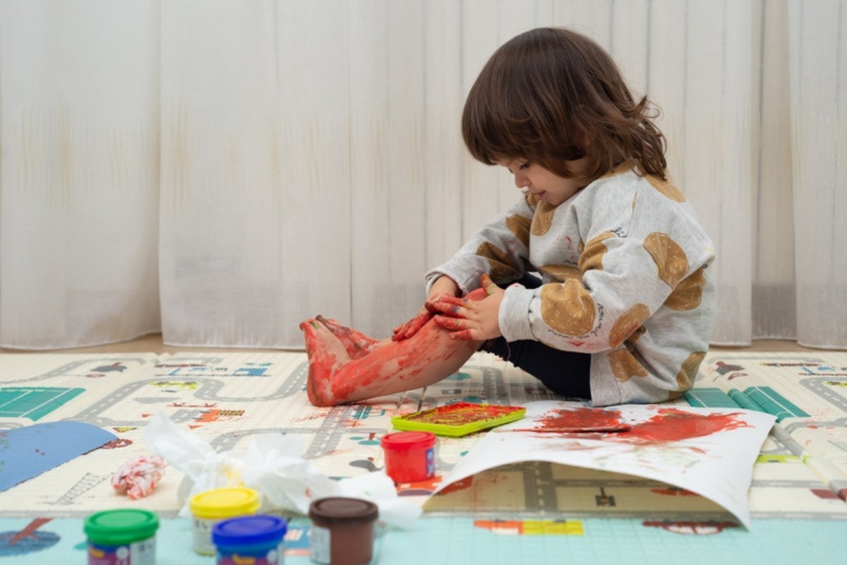 Toddler sitting on a play mat with paint on her hands and feet during a painting activity