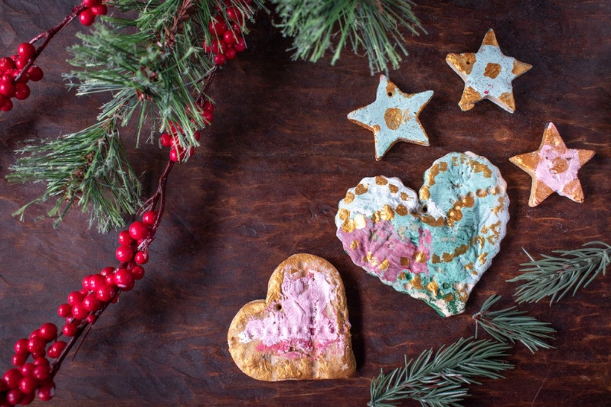 Painted salt dough Christmas ornaments shaped like hearts and stars on a wooden table