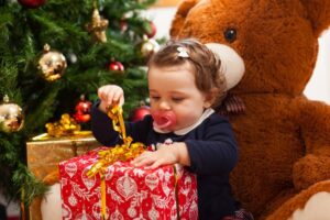 Toddler opening a red Christmas present next to the tree