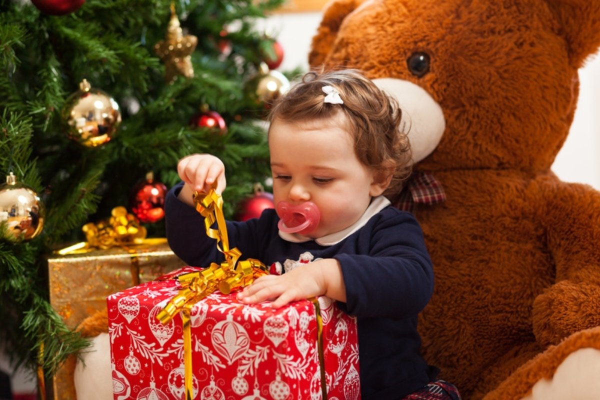 Toddler opening a red Christmas present next to the tree